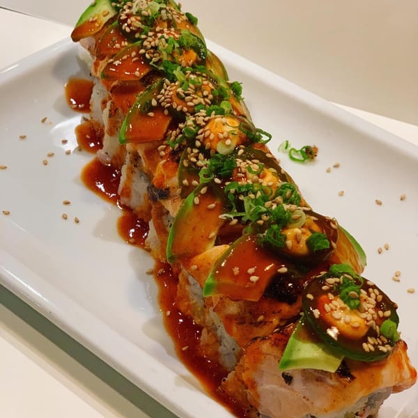 Edomasa Sushi Bar & Restaurant's sushi roll topped with avocado, sauce, sesame seeds, and green onions.