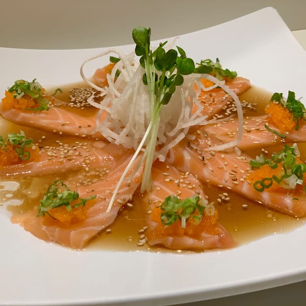 Salmon sashimi with roe, scallions, sesame seeds, and daikon radish in a light sauce.