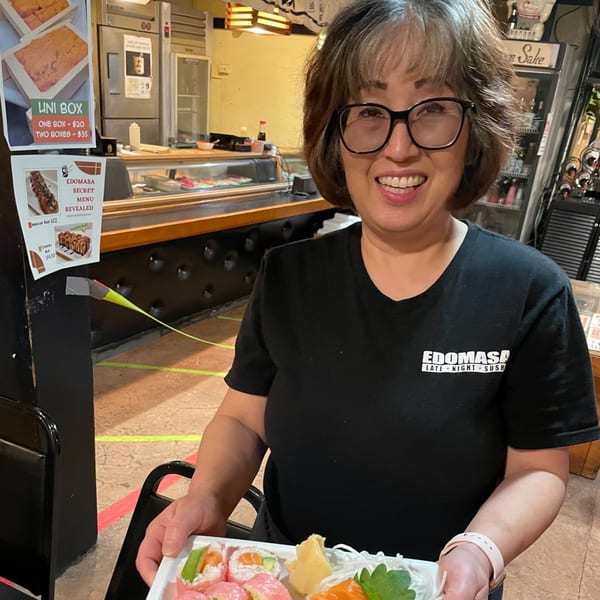Smiling Edomasa staff member holding a plate of sushi, including pink and salmon rolls.