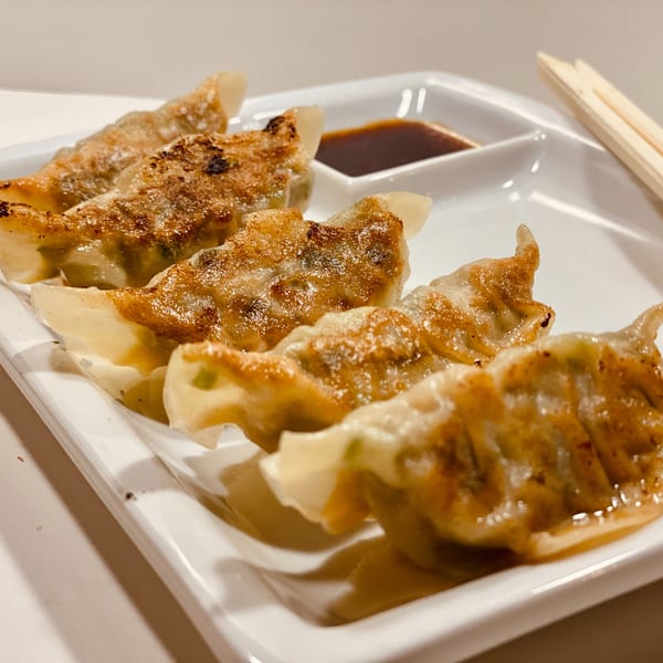 Crispy pan-fried gyoza dumplings with dipping sauce and chopsticks on a white plate.