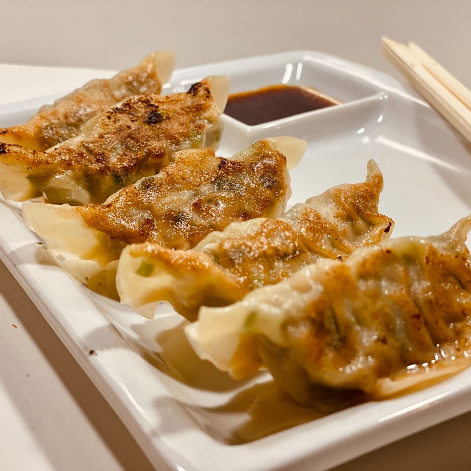 Crispy pan-fried gyoza dumplings with dipping sauce and chopsticks on a white plate.