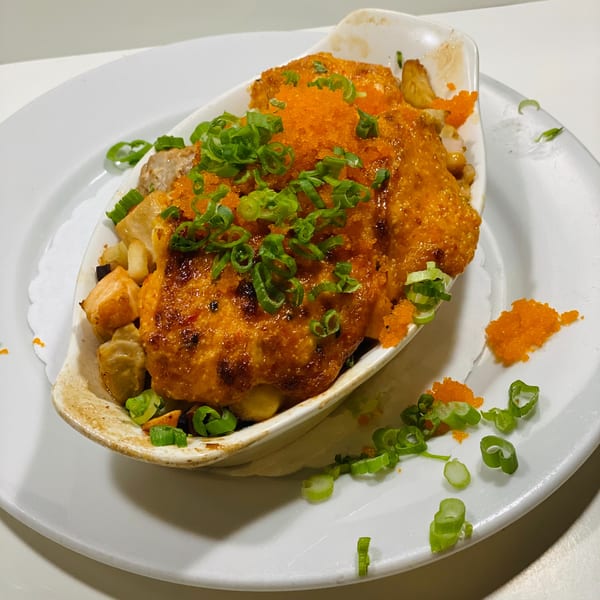 Baked seafood dish topped with bright orange roe and green onions, served in a white boat-shaped dish.