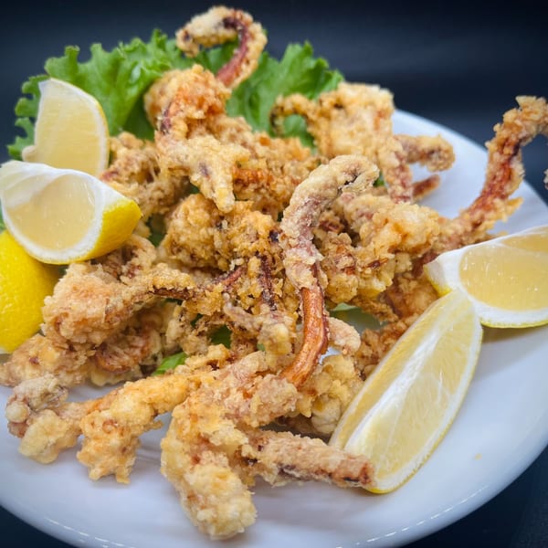Crispy fried soft-shell crab, garnished with fresh lettuce and lemon wedges, on a white plate.